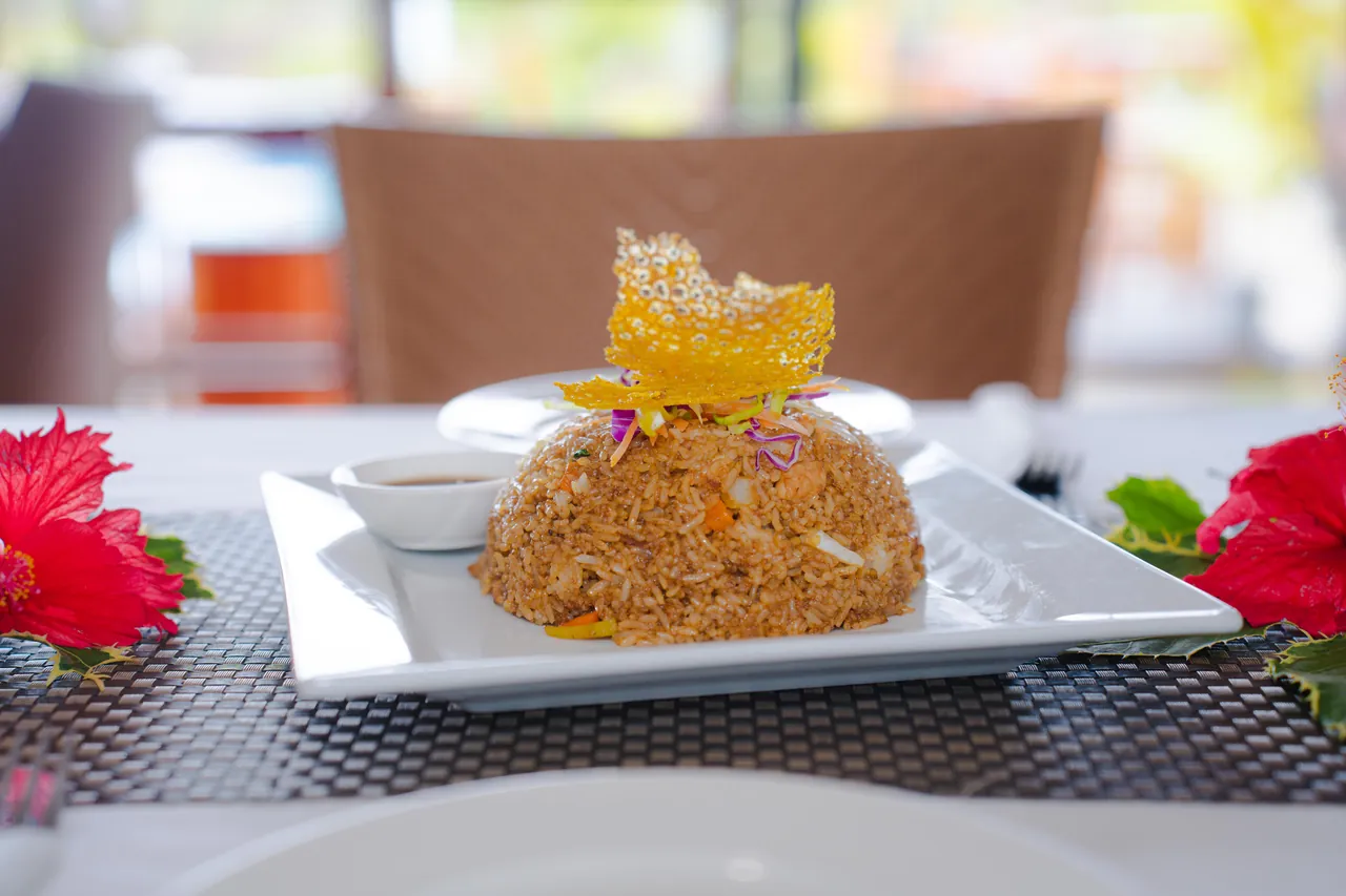 Fried rice plated with a crisp garnish and a side of sauce