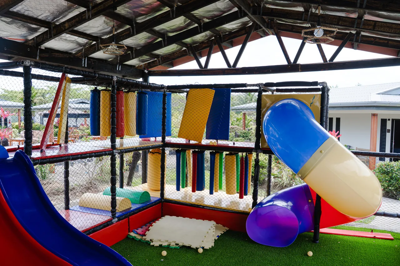 A blue and yellow tube slide and climbing structure under the Playland roof